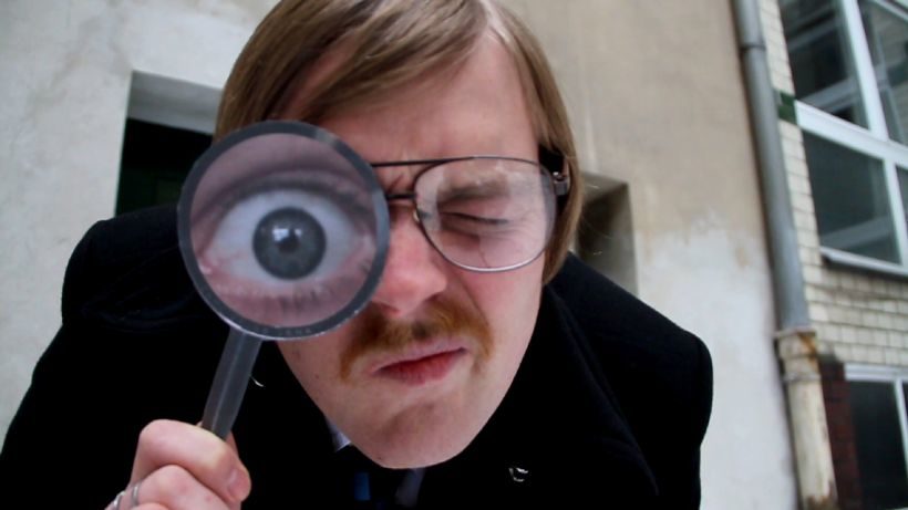 Film Nun sehen Sie Folgendes: Ein Mann mit Brille und Schnurrbart schaut durch eine Lupe. Sein rechtes Auge wird durch die Lupe stark vergrößert.