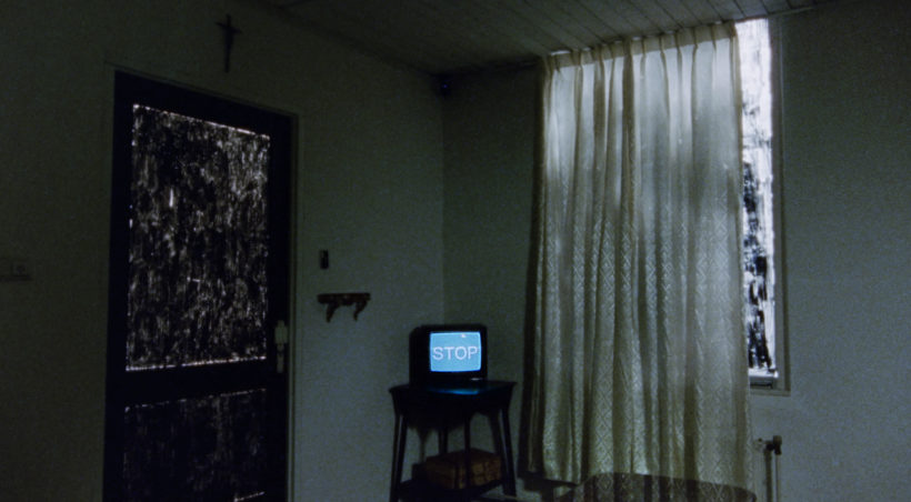 Filmstill ONE HOUR REAL: Ein abgedunkeltes Zimmer, zugezogene Vorhänge, im Zentrum ein alter Fernseher, auf dem das Wort STOP geschrieben steht.